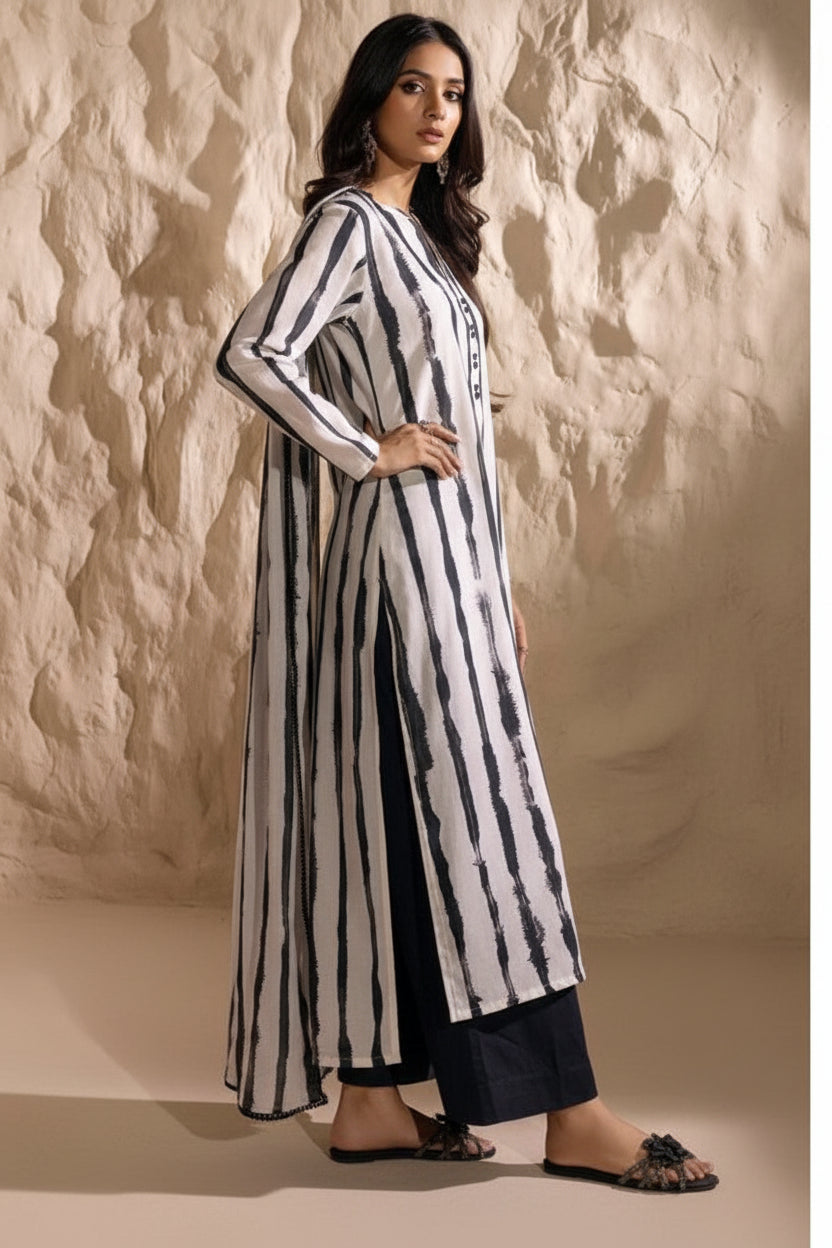 Woman wearing a black and white striped outfit with a long duster, sitting on a chair against a beige wall.